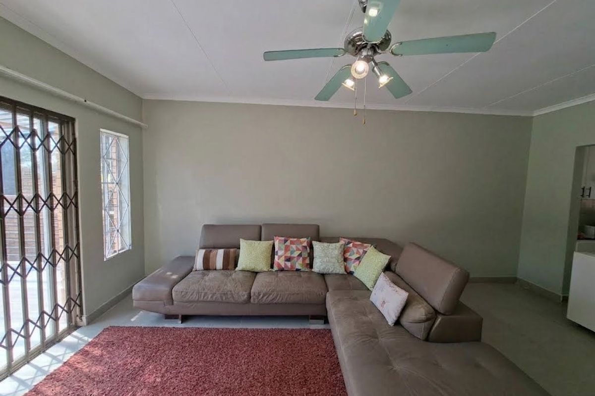 A spacious living room featuring tiled flooring, a ceiling fan, and a security gate leading to the exterior.