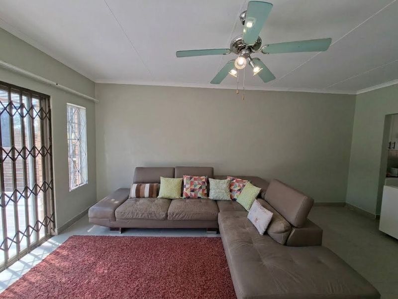 A spacious living room featuring tiled flooring, a ceiling fan, and a security gate leading to the exterior.