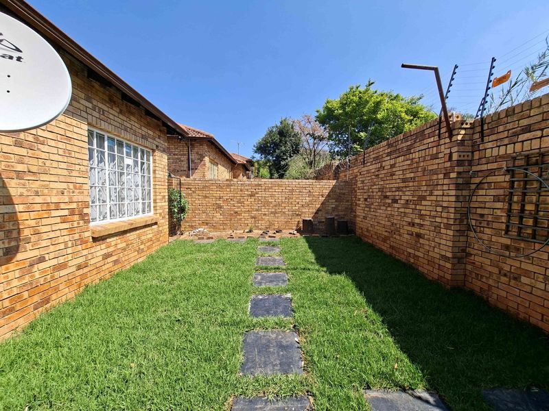 A private rear garden area featuring a well-maintained lawn, stone pathway, and secure face brick boundary walls with electric fencing.