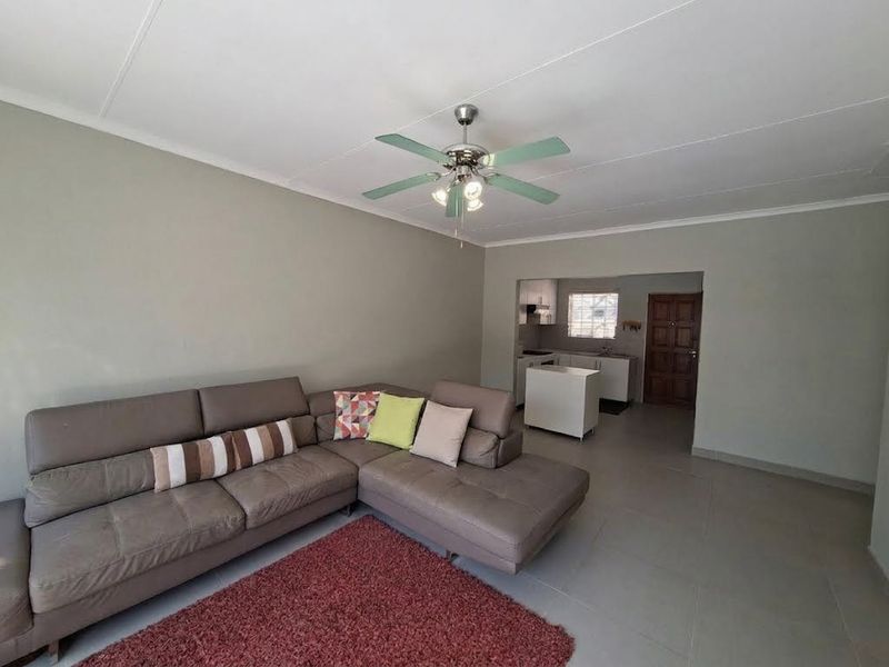 Open-plan living area featuring neutral wall tones, tiled flooring, and a ceiling fan, with a view through to the kitchen and entrance door.