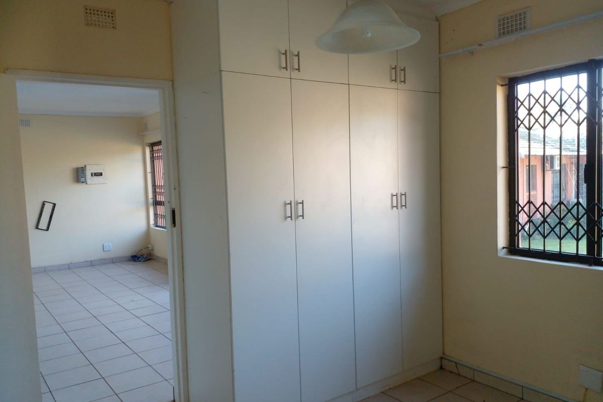 A vacant bedroom featuring built-in wardrobes, tiled flooring, and a security gate on the window, offering a functional and neutral living space.