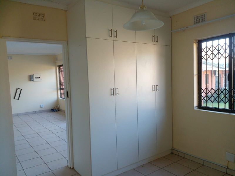 A vacant bedroom featuring built-in wardrobes, tiled flooring, and a security gate on the window, offering a functional and neutral living space.