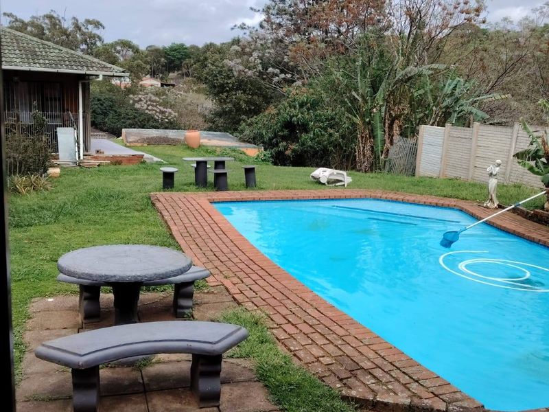 Outdoor pool area featuring a swimming pool with brick surround, paved patio space, and a surrounding garden with precast boundary walling.