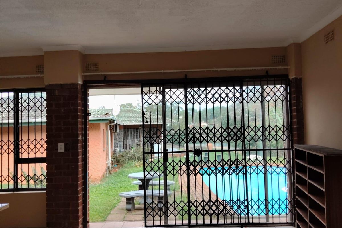 Spacious living area featuring tiled floors and a large sliding door with security gate, offering direct access to the garden and pool area.