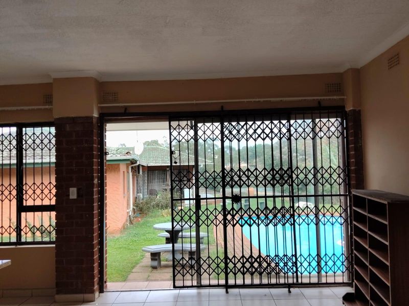 Spacious living area featuring tiled floors and a large sliding door with security gate, offering direct access to the garden and pool area.
