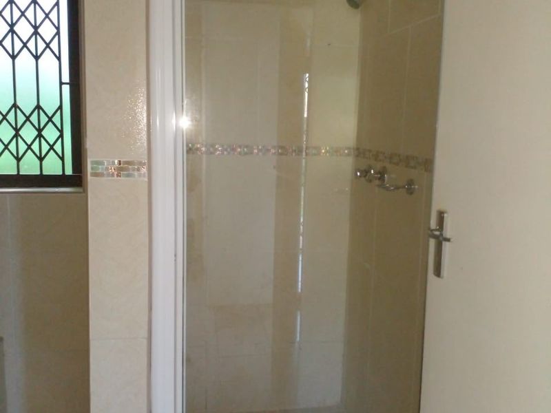 A functional bathroom featuring a glass-enclosed shower with tiled walls and flooring, complemented by a window with a security gate.
