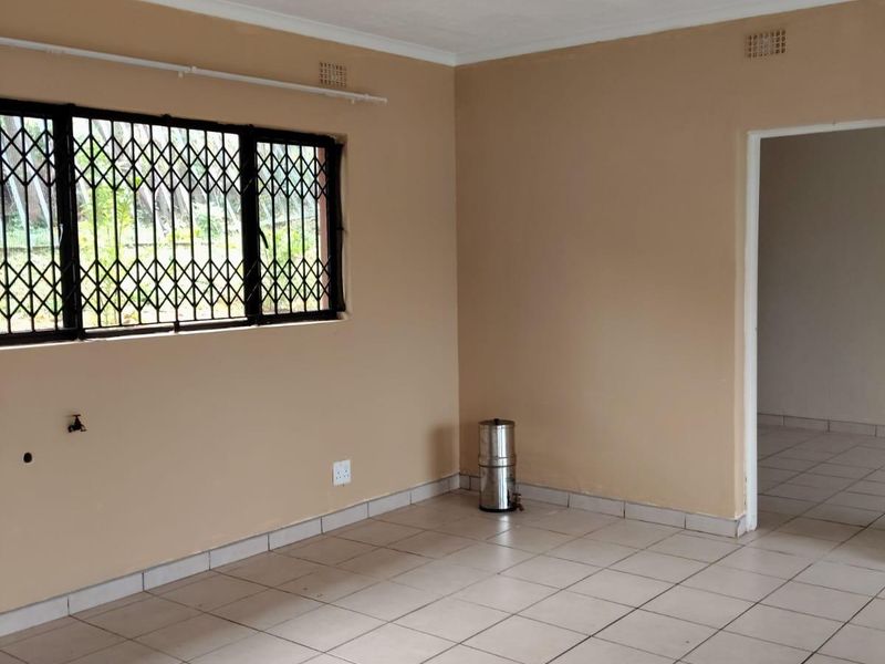 A spacious, empty living area featuring neutral wall paint, tiled flooring, and a window fitted with a security gate.