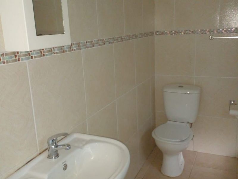 A functional bathroom featuring a pedestal washbasin, toilet, and neutral wall tiling with a decorative mosaic border.