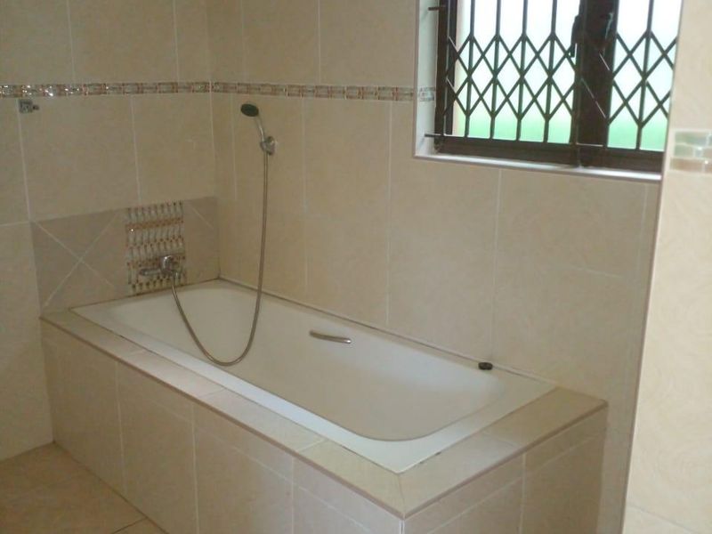 A clean, neutral-toned bathroom featuring a built-in bathtub with a shower mixer and tiled finishes throughout.