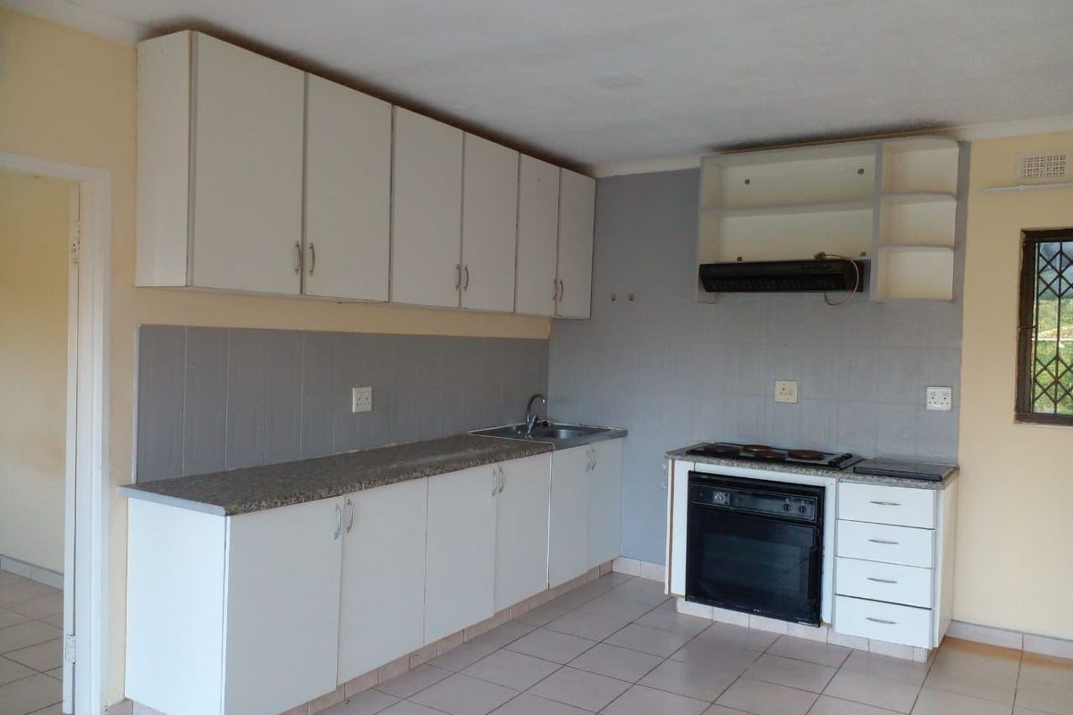 A functional kitchen featuring white cabinetry, laminate countertops, built-in oven, hob, and extractor fan, with tiled flooring and backsplash throughout.