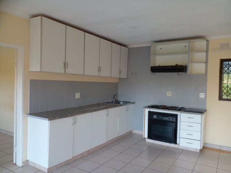 A functional kitchen featuring white cabinetry, laminate countertops, built-in oven, hob, and extractor fan, with tiled flooring and backsplash throughout.
