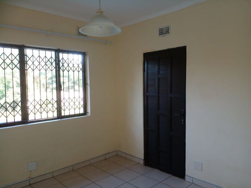 An empty bedroom featuring tiled flooring, a window with a security gate, and a dark-toned interior door.