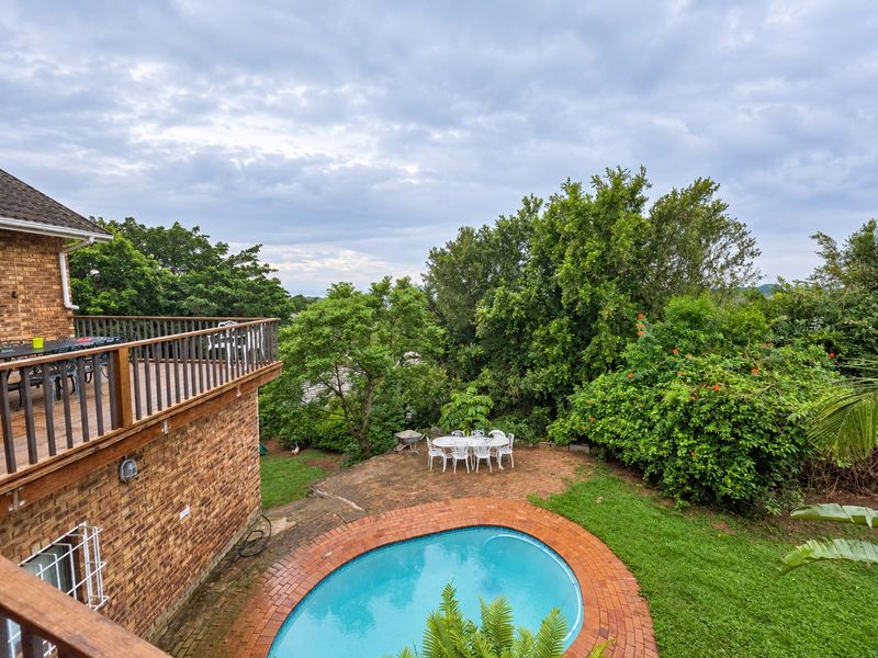 Outdoor area featuring a swimming pool with brick coping, a raised wooden deck with balustrades, and a landscaped garden setting.