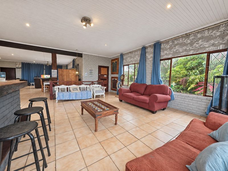 Spacious open-plan living area featuring tiled floors, painted brick walls, timber ceilings, and a built-in bar counter with large windows overlooking the garden.