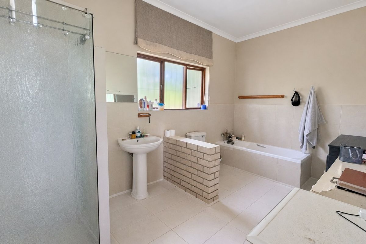 A functional bathroom featuring a pedestal basin, a built-in bathtub, and a separate glass-enclosed shower with neutral tiled finishes.