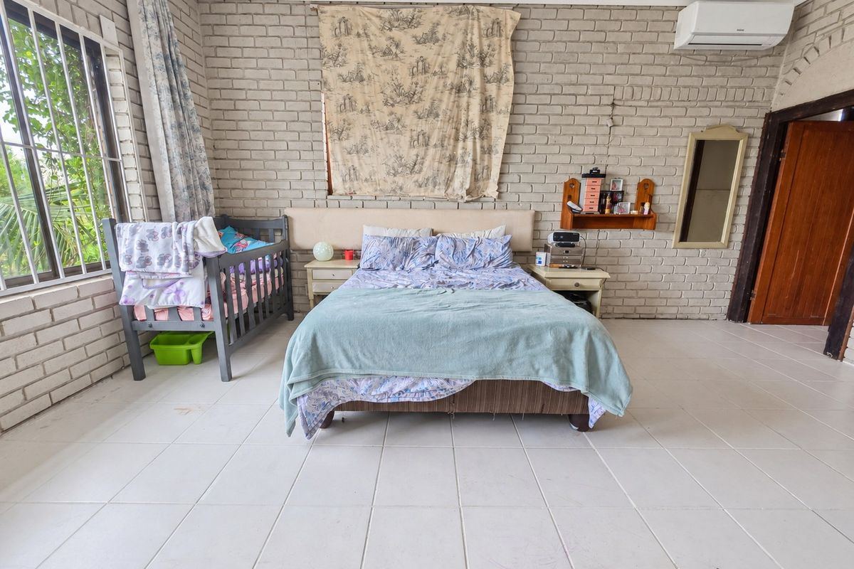 Spacious bedroom featuring exposed brick walls, ceramic tiled flooring, and a wall-mounted air conditioning unit.