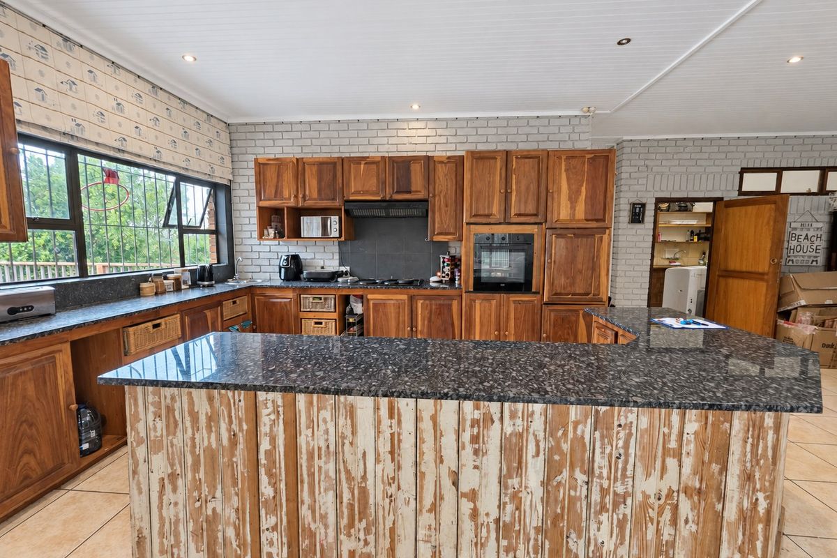 Spacious kitchen featuring granite countertops, extensive wooden cabinetry, built-in oven, and a unique distressed-finish island, set against a classic brick feature wall.