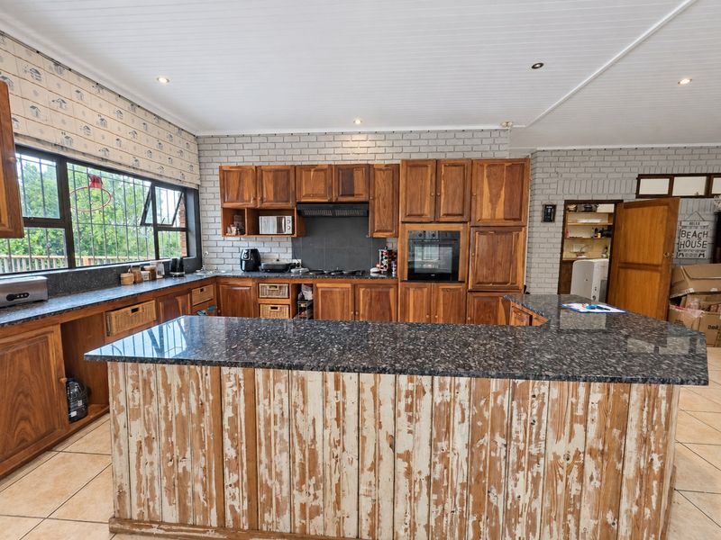 Spacious kitchen featuring granite countertops, extensive wooden cabinetry, built-in oven, and a unique distressed-finish island, set against a classic brick feature wall.