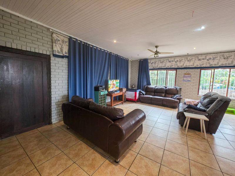 Spacious living room featuring painted brick walls, tiled flooring, and a ceiling fan, offering a comfortable and functional family space.
