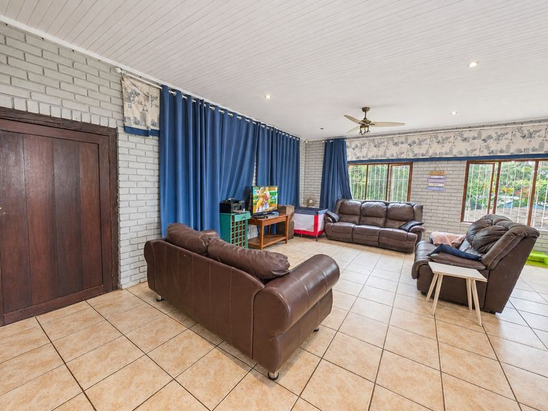 Spacious living room featuring painted brick walls, tiled flooring, a ceiling fan, and large windows allowing for natural light.
