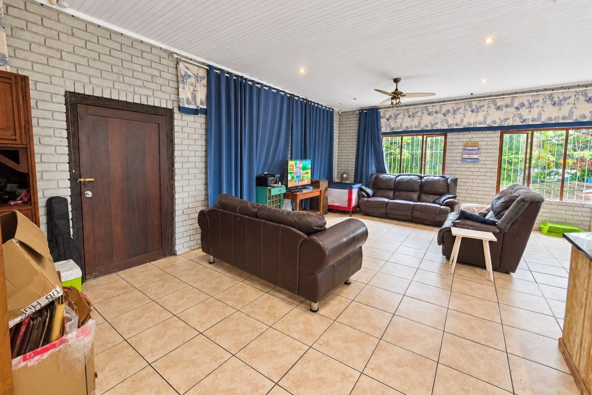 Spacious living room featuring exposed brick walls, tiled flooring, and a ceiling fan, offering a comfortable and functional layout.