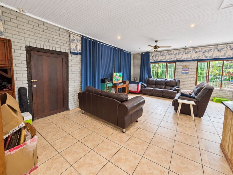 Spacious living room featuring exposed brick walls, tiled flooring, and a ceiling fan, offering a comfortable and functional layout.