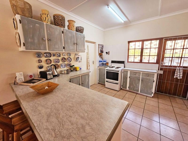 A functional kitchen featuring laminate countertops, built-in cabinetry, a freestanding electric stove, and tiled flooring with direct access to the exterior.