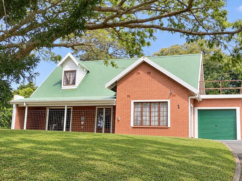 Front view of a charming brick house featuring a green corrugated metal roof, a single garage, a carport, and a well-maintained lawn.