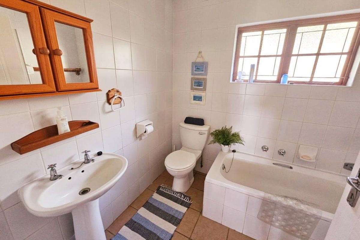 A functional bathroom featuring a pedestal basin, built-in bathtub, and toilet, finished with neutral wall and floor tiling.