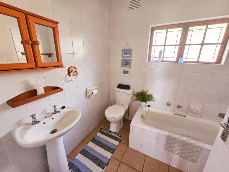 A functional bathroom featuring a pedestal basin, built-in bathtub, and toilet, finished with neutral wall and floor tiling.