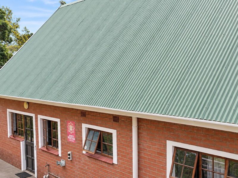 A view of the rear exterior featuring a green corrugated metal roof, red brick walls, and white-framed casement windows.
