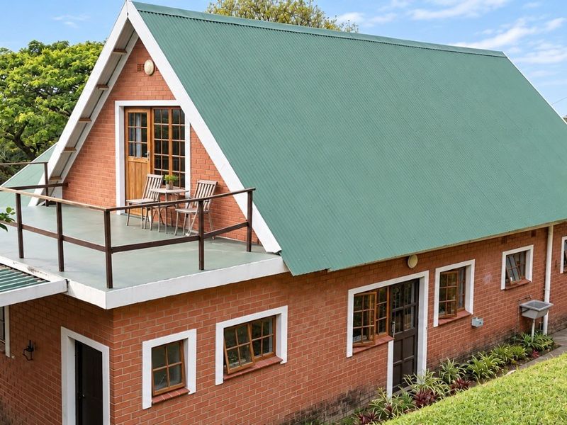 Rear view of a two-story brick house featuring a green corrugated metal roof and an upper-level balcony with timber-framed windows.