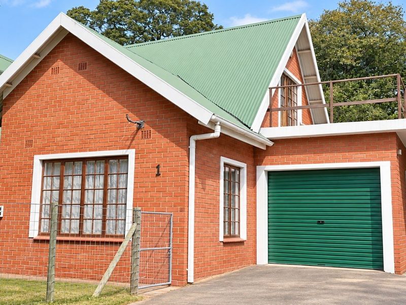 Front view of a charming red brick house featuring a green corrugated metal roof, a single garage, and an attached carport.