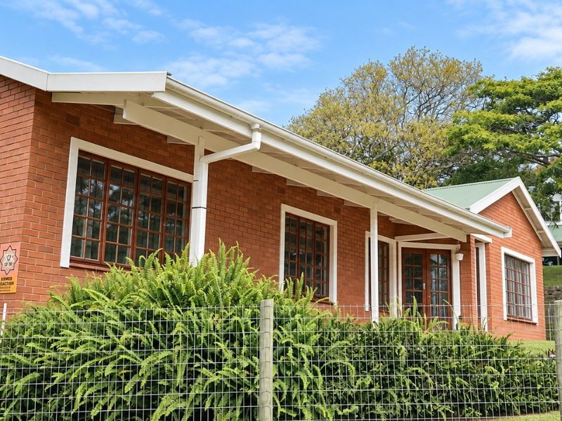A well-maintained single-story face brick house featuring timber-framed windows and doors, set within a landscaped garden with wire mesh perimeter fencing.