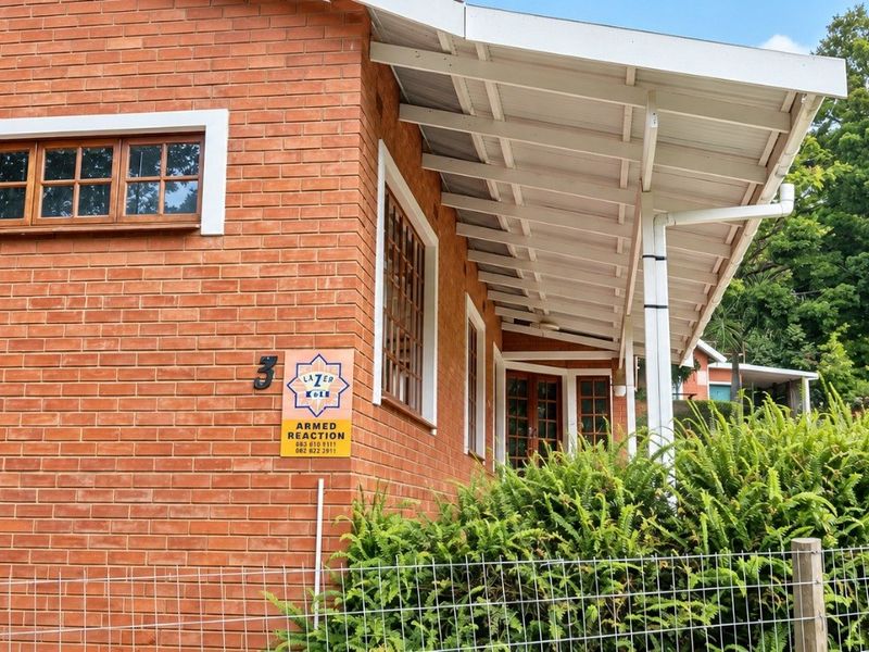 A side view of a red brick house featuring timber-framed windows and a covered patio area with a well-maintained garden.