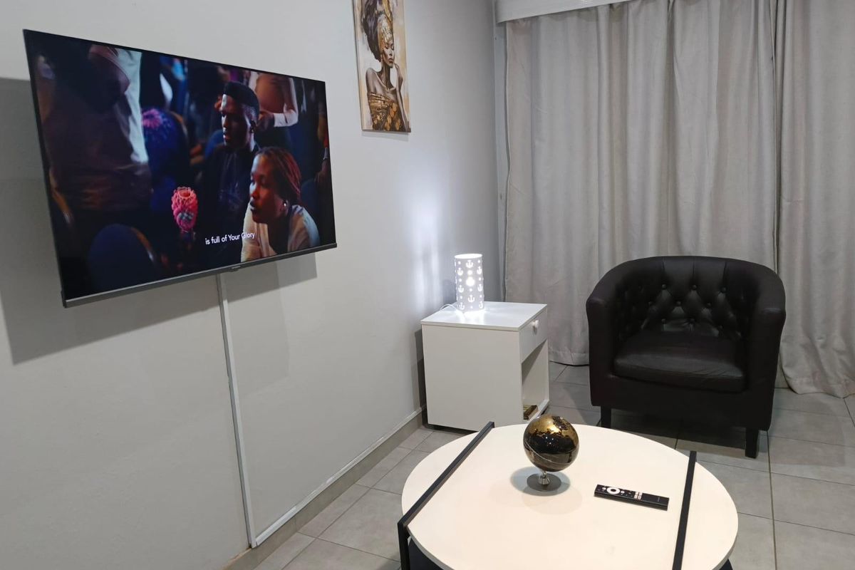 A compact living room area featuring neutral wall finishes, tiled flooring, and a wall-mounted television setup.