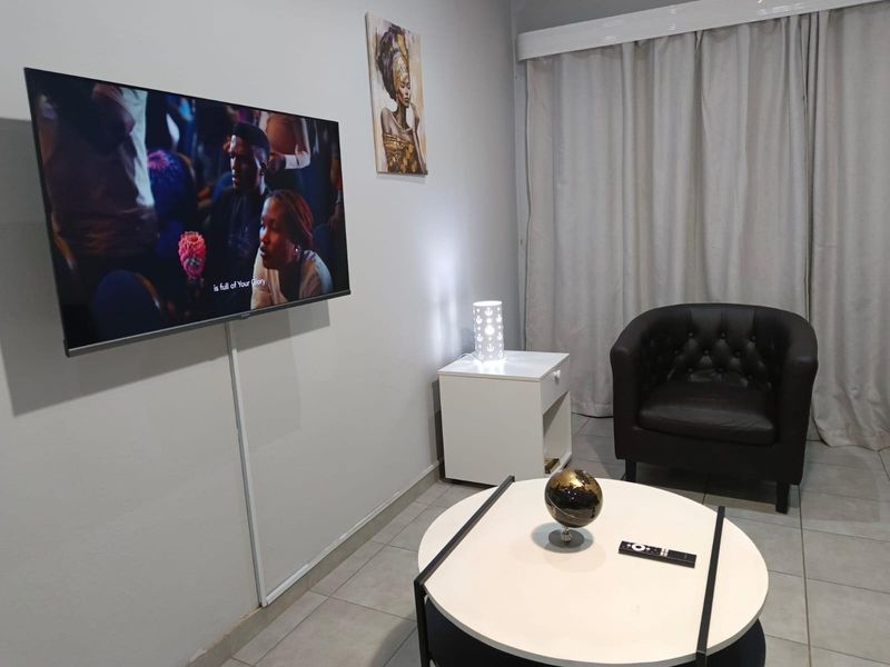 A compact living room area featuring neutral wall finishes, tiled flooring, and a wall-mounted television setup.