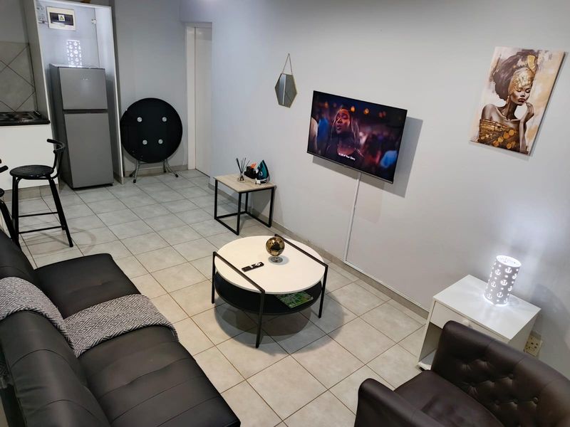 Open-plan living area featuring tiled flooring and a compact kitchen corner with built-in cabinetry and integrated cooking appliances.
