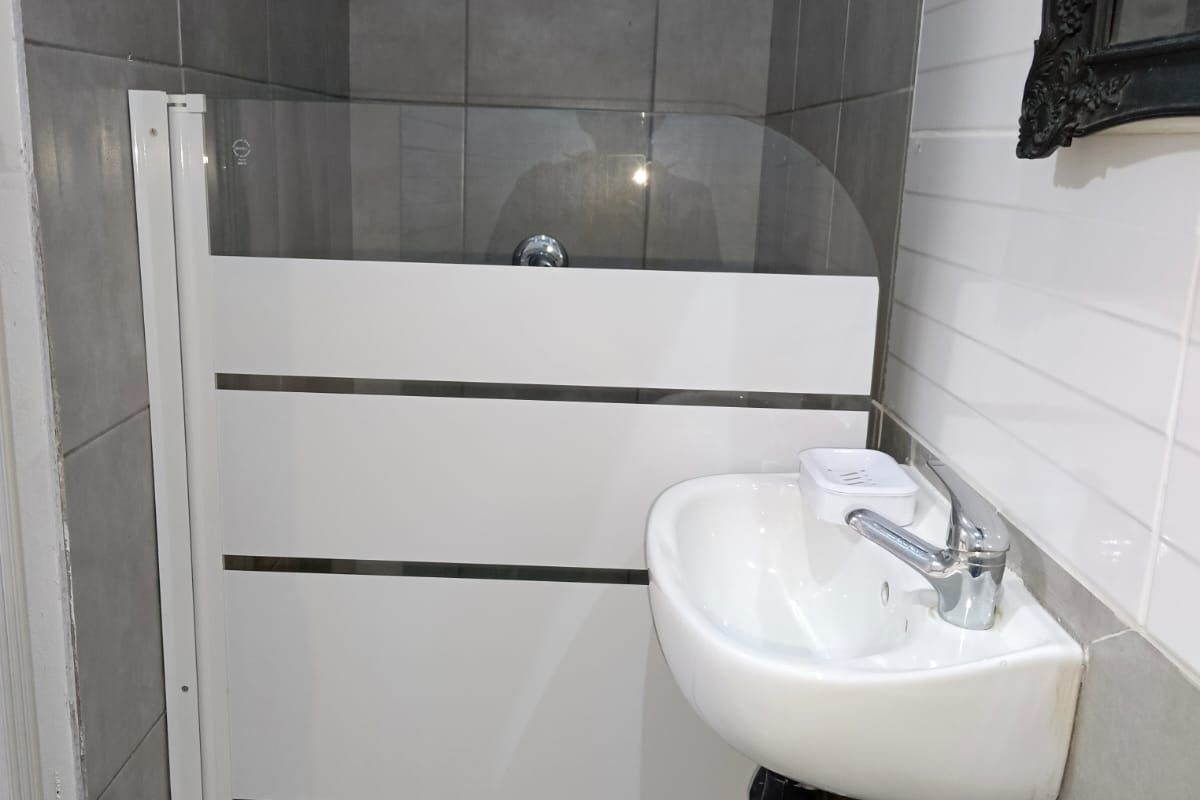 Compact bathroom featuring a wall-mounted basin, mixer tap, and a tiled shower enclosure with a glass screen.