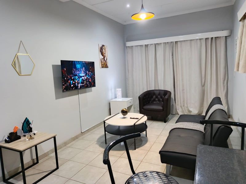 A functional living room featuring neutral tiled flooring, a central pendant light, and a wall-mounted television setup.