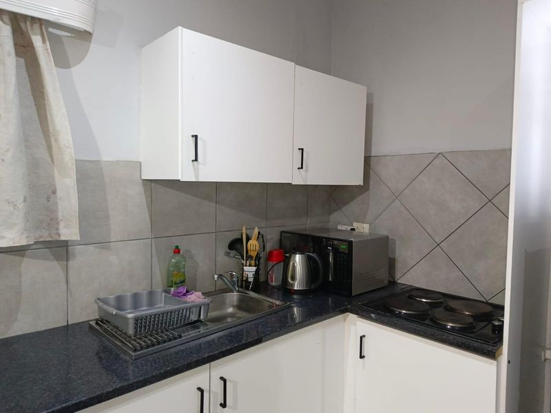 Compact kitchen featuring white cabinetry, dark laminate countertops, a stainless steel sink, and a built-in electric hob with a tiled backsplash.