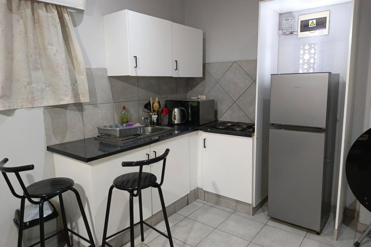 Compact kitchen featuring white cabinetry, granite countertops, tiled backsplash, and an integrated electric hob, with an exposed electrical distribution board.