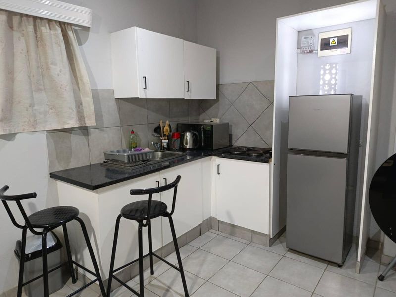 Compact kitchen featuring white cabinetry, granite countertops, tiled backsplash, and an integrated electric hob, with an exposed electrical distribution board.