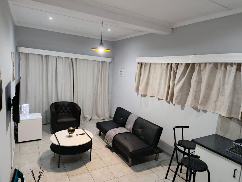 An open-plan living area featuring tiled flooring, recessed lighting, and a functional kitchen corner, offering a versatile space for relaxation and dining.