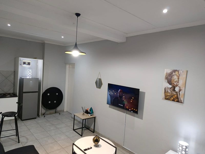 An open-plan living area featuring tiled flooring, recessed lighting, and a modern kitchen corner with built-in cabinetry.