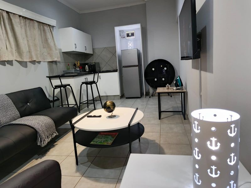Open-plan living area featuring tiled flooring, a compact kitchen with built-in cabinetry, and a wall-mounted television.