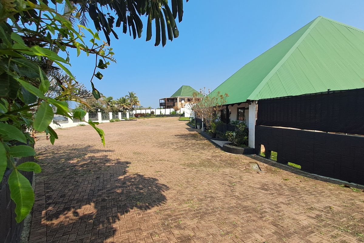 Spacious paved rear exterior area featuring a perimeter wall and a building with a green metal roof.