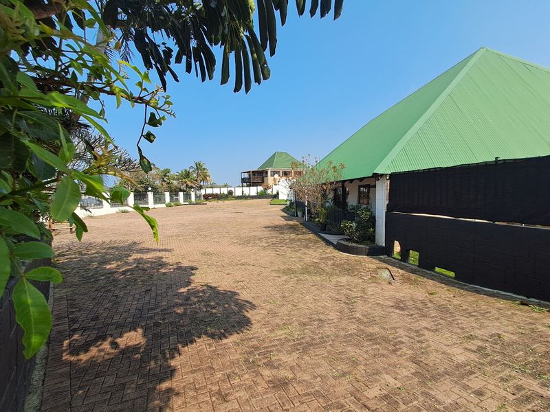 Spacious paved rear exterior area featuring a perimeter wall and a building with a green metal roof.
