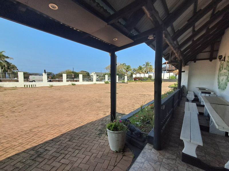 A spacious covered outdoor patio area featuring timber support posts, built-in bench seating, and a large paved courtyard enclosed by security fencing.