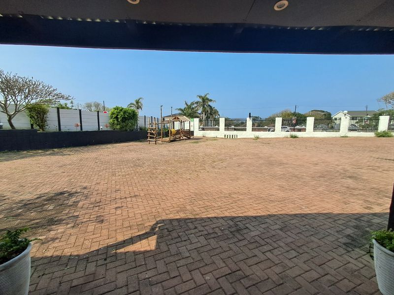 A spacious paved outdoor courtyard area featuring perimeter walling and security fencing, viewed from a covered patio space.